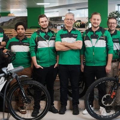 Team in grüner Arbeitskleidung in einem Fahrradgeschäft mit E-Bikes