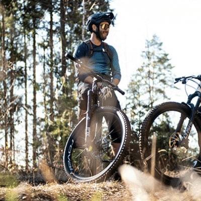 Zwei Personen mit Mountainbikes im Wald bei sonnigem Wetter
