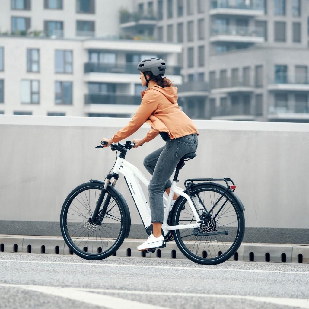 Fahrerin auf einem Riese & Müller E-Bike fährt vor einer modernen Neubau-Skyline. Ideal für urbane Mobilität und st