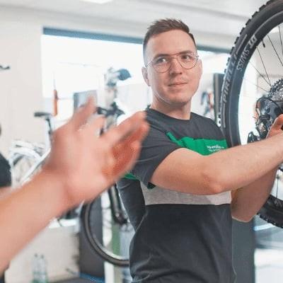 Mitarbeiter wartet Fahrrad in Werkstatt mit Ersatzteilen im Hintergrund