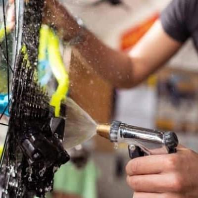 Mann reinigt Fahrradkette mit Wasserstrahl im Frühling