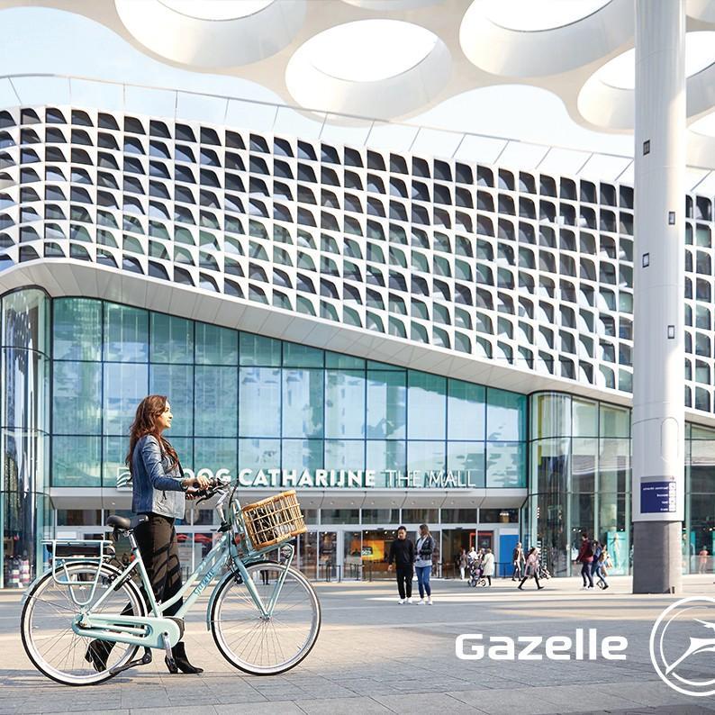 Eine Frau schiebt das Gazelle e-Bike Miss Grace vor einem Bahnhof entlang