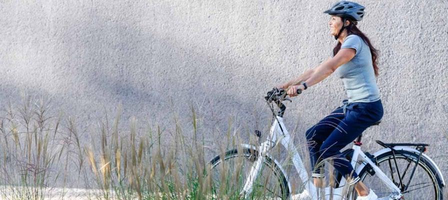 Frau auf E-Bike fährt vor grauer Wand mit Gras im Vordergrund