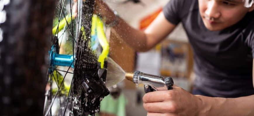 Mann reinigt Fahrradkette mit Wasserstrahl im Frühling