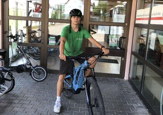 Junger Mann mit Helm auf E-Bike vor Geschäftseingang
