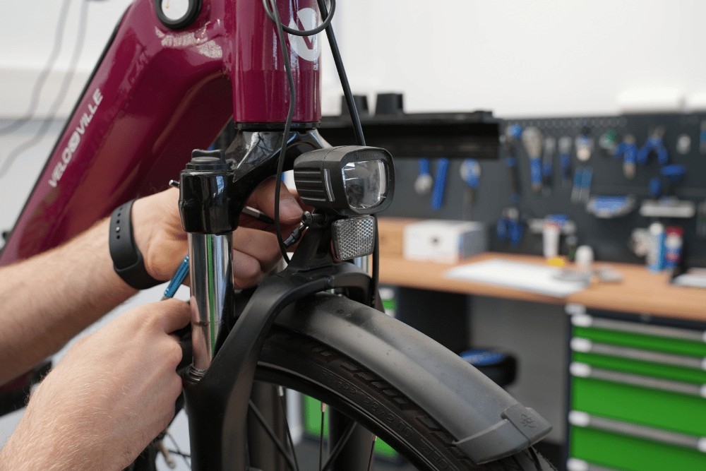 Das Bild zeigt eine Person, die an einem e-Bike arbeitet, um die Beleuchtung zu überprüfen