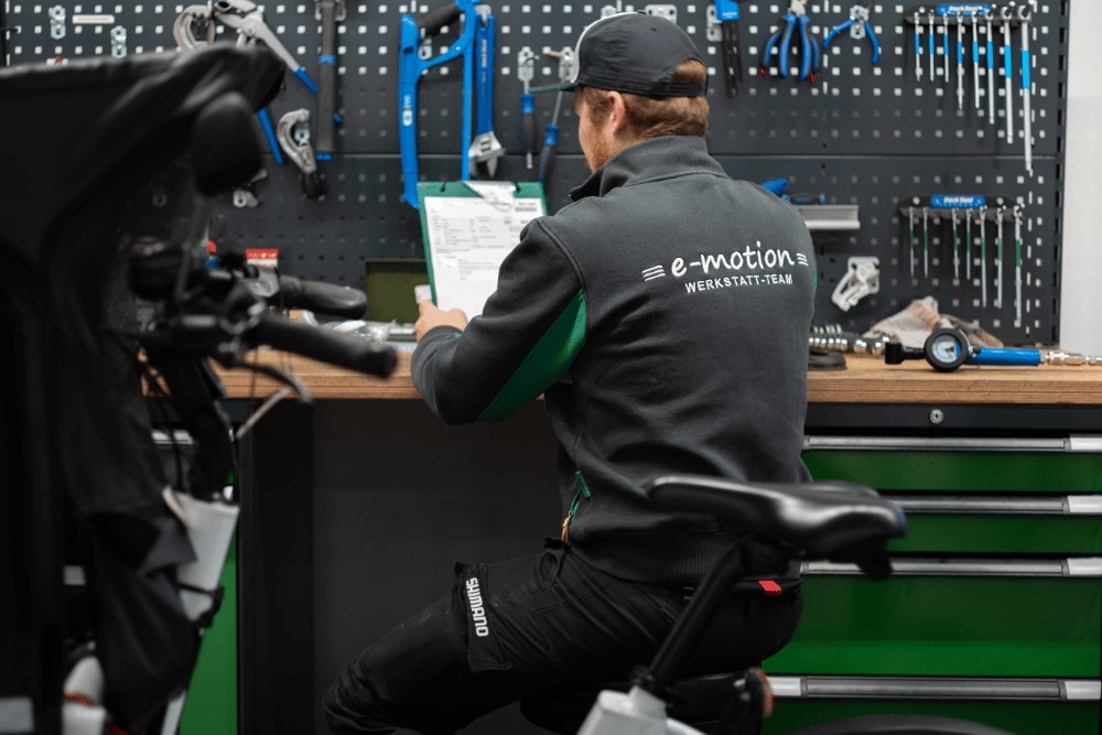 Ein Werkstattmitarbeiter sitzt in der Werkstatt an der Werkbank, in der Hand hält er eine Mappe
