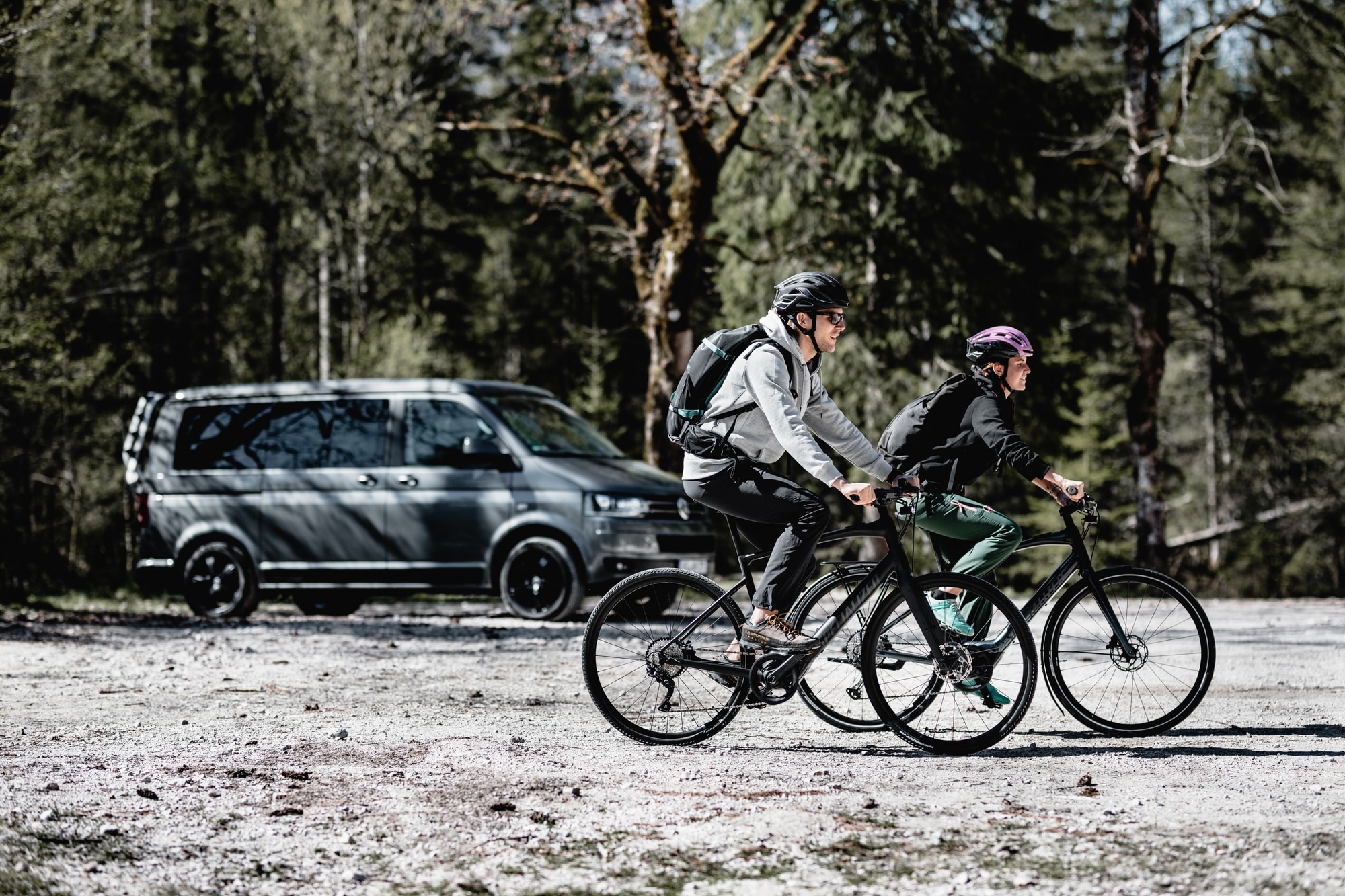 Zwei Personen fahren auf e-Bikes durch die Natur, im Hintergrund sieht man einen Transporter