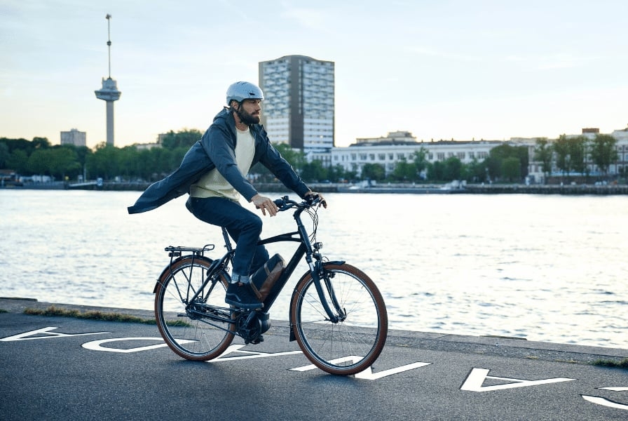 Mann auf Riese & Müller Cruiser E-Bike am Flussufer bei Sonnenuntergang