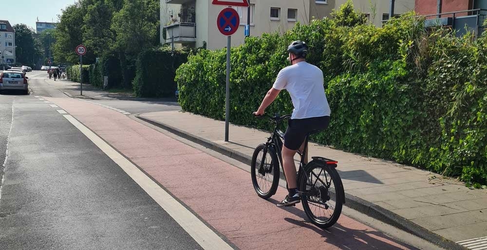 Radfahrer auf Radweg mit Verkehrsschildern und grüner Hecke