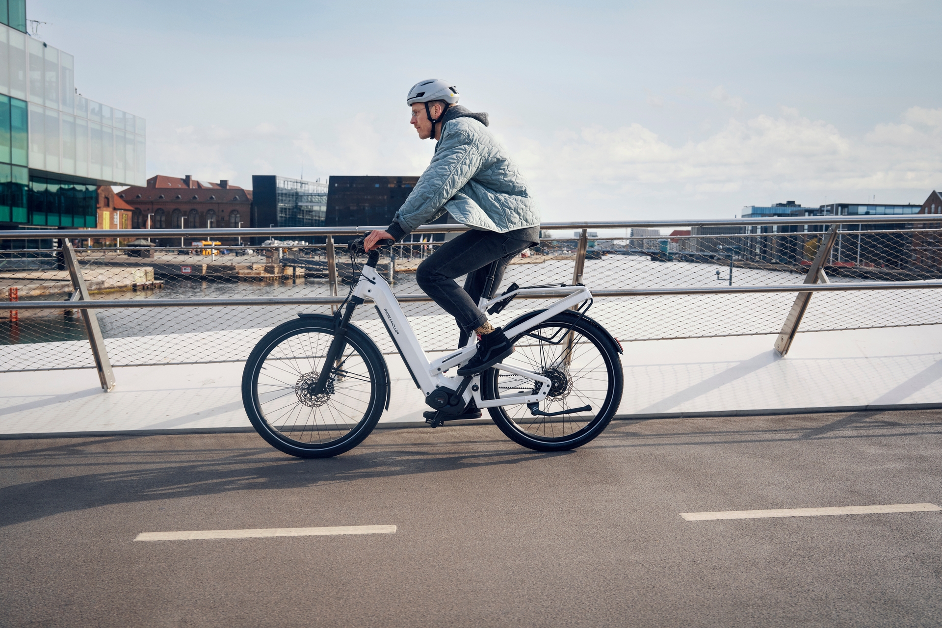 Person fährt mit einem weißen Riese & Müller Homage4 e-Bike über eine Brücke in urbaner Umgebung.