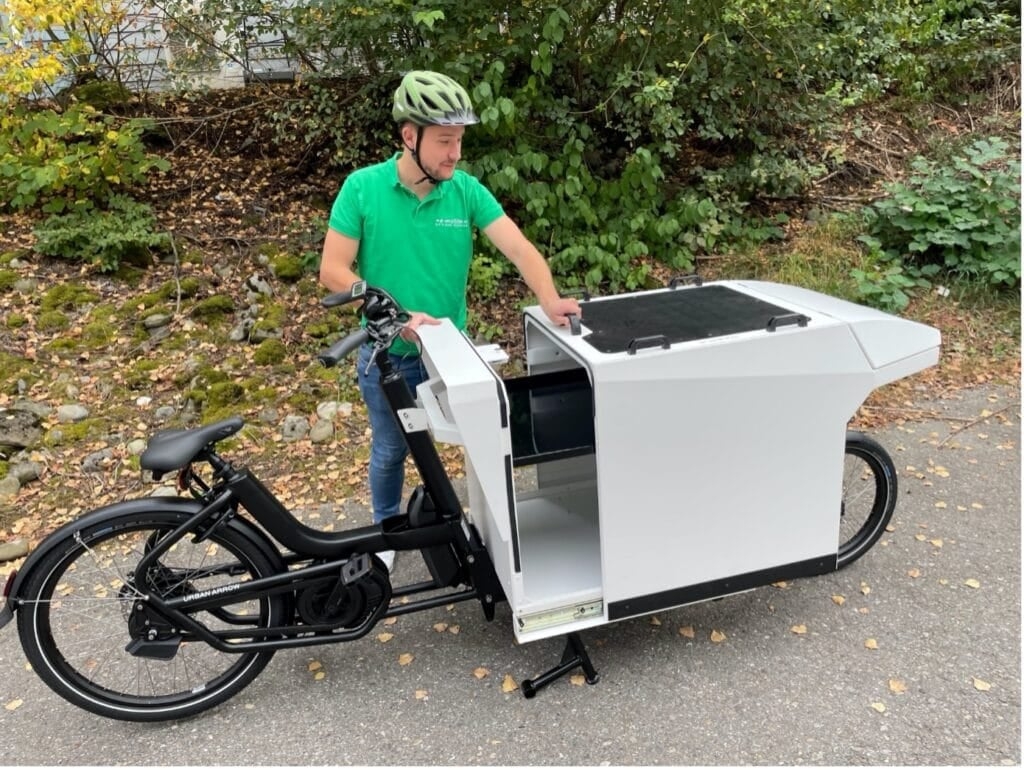Mann mit Cargo-E-Bike auf Straße vor grüner Kulisse