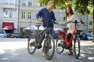 Mann und Frau mit E-Bikes im urbanen Umfeld