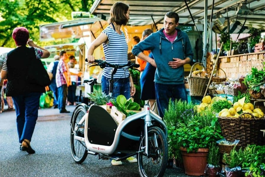 Personen mit Lastenfahrrad auf einem Markt mit frischem Obst und Gemüse