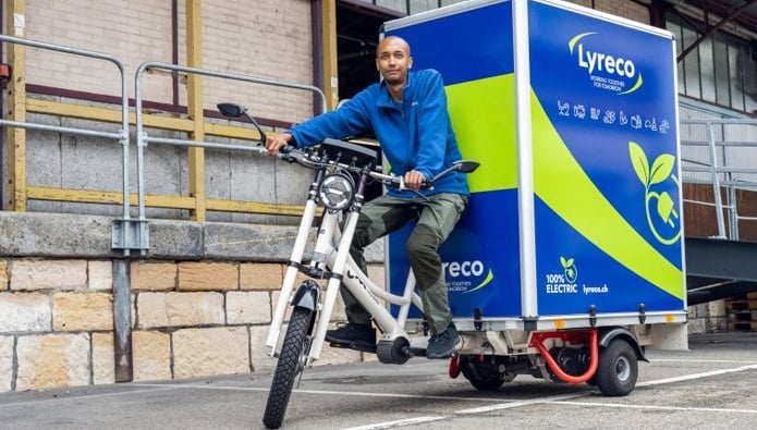 Lyreco Lastenradfahrer mit elektrisch unterstütztem Cargo-Bike vor Lagerhaus