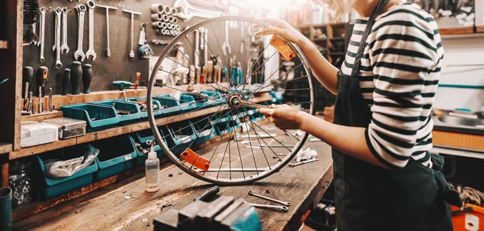 Das Bild zeigt eine Werkstatt, in der ein Mechaniker an einem Fahrradrad arbeitet.