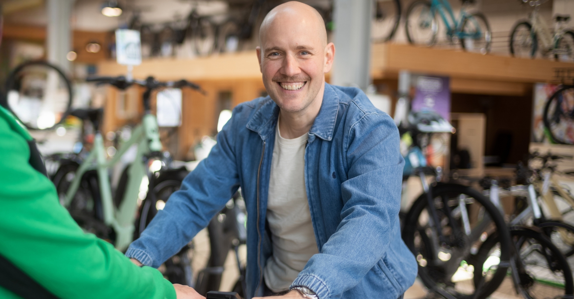 Zwei Männer stehen in einem Fahrradgeschäft. Der Mann in der blauen Jacke sitzt auf einem e-Bike und lächelt in die