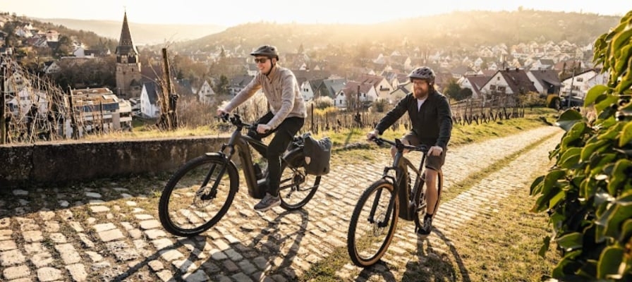 Zwei Personen auf E-Bikes fahren auf einem gepflasterten Weg bei Sonnenuntergang