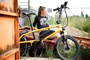 Frau sitzt auf gelbem E-Bike vor urbanem Hintergrund