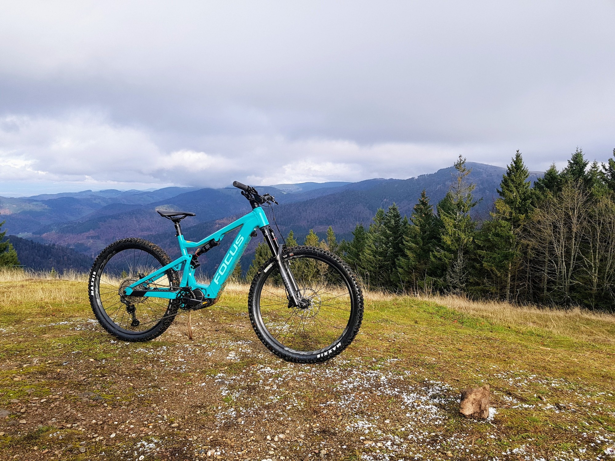 Das Bild zeigt das E-Bike Focus Jam² 7.8 auf einem hügeligen Gelände, umgeben von einer Waldlandschaft und Bergen.