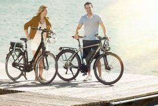 Zwei Personen mit E-Bikes auf einem Holzsteg am Wasser