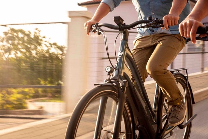 Person fährt Riese & Müller E-Bike auf sonniger Straße