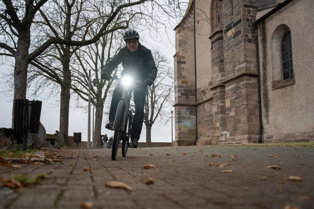 Mann auf E-Bike fährt bei Herbstwetter an historischer Kirche vorbei