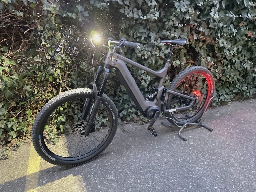 E-Bike mit eingeschaltetem Front- und Rücklicht auf Asphaltweg vor Hecke