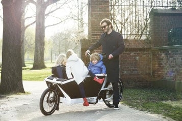 Mann fährt Urban Arrow Lasten-E-Bike mit Kindern im Park