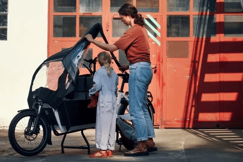 Frau und Kind mit Lastenrad vor rotem Tor