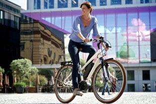 Frau auf E-Bike mit Bosch-Akku vor moderner Glasfassade