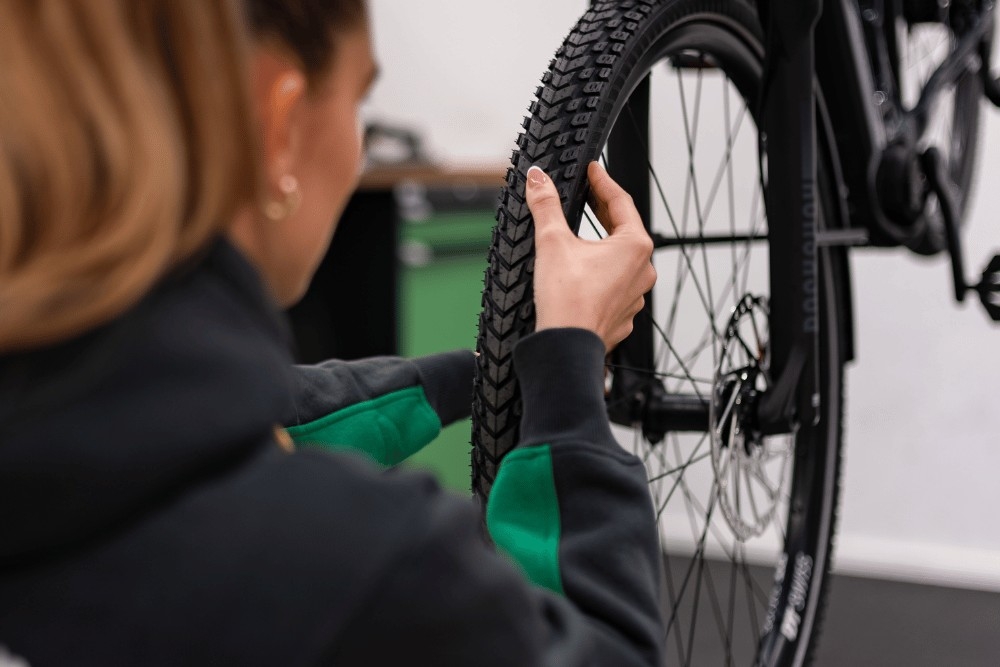 Das Bild zeigt eine Person, die den Reifen eines e-Bikes überprüft.