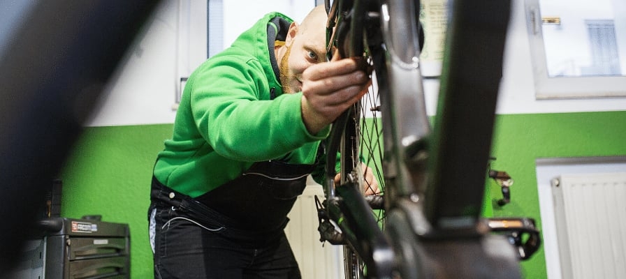 Mechaniker inspiziert Fahrrad in Werkstatt mit grünem Hintergrund